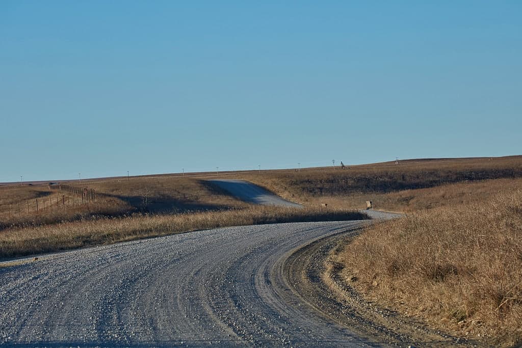 A gravel road curving through open prairie under a clear sky