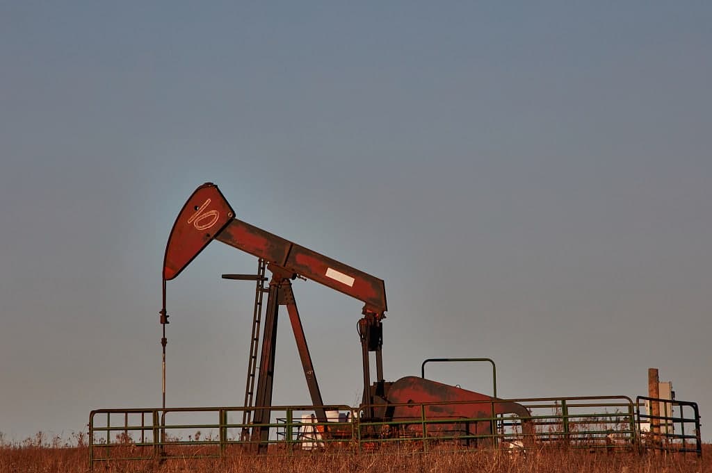 A red pumpjack standing behind a pipe fence in tallgrass prairie at dusk, Osage County
