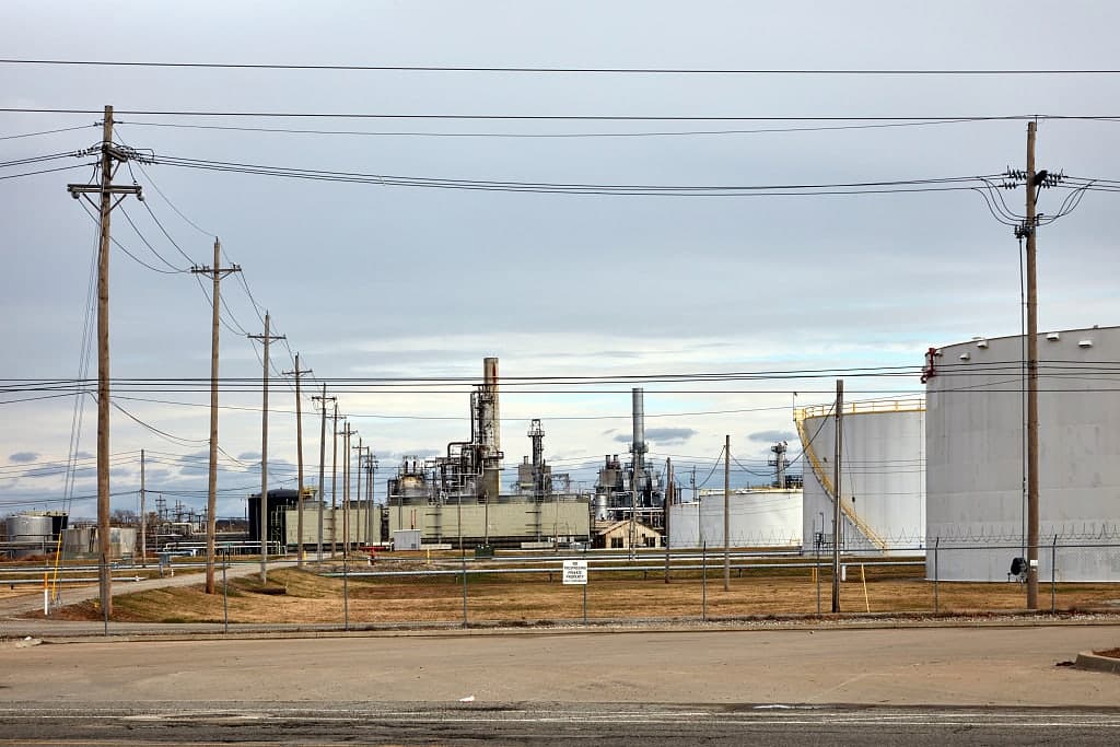 Power lines and poles crossing in front of a refinery and storage tanks in Tulsa, Oklahoma