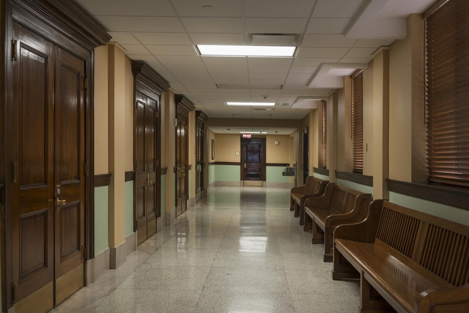 An empty government corridor lined with tall wooden doors and waiting benches