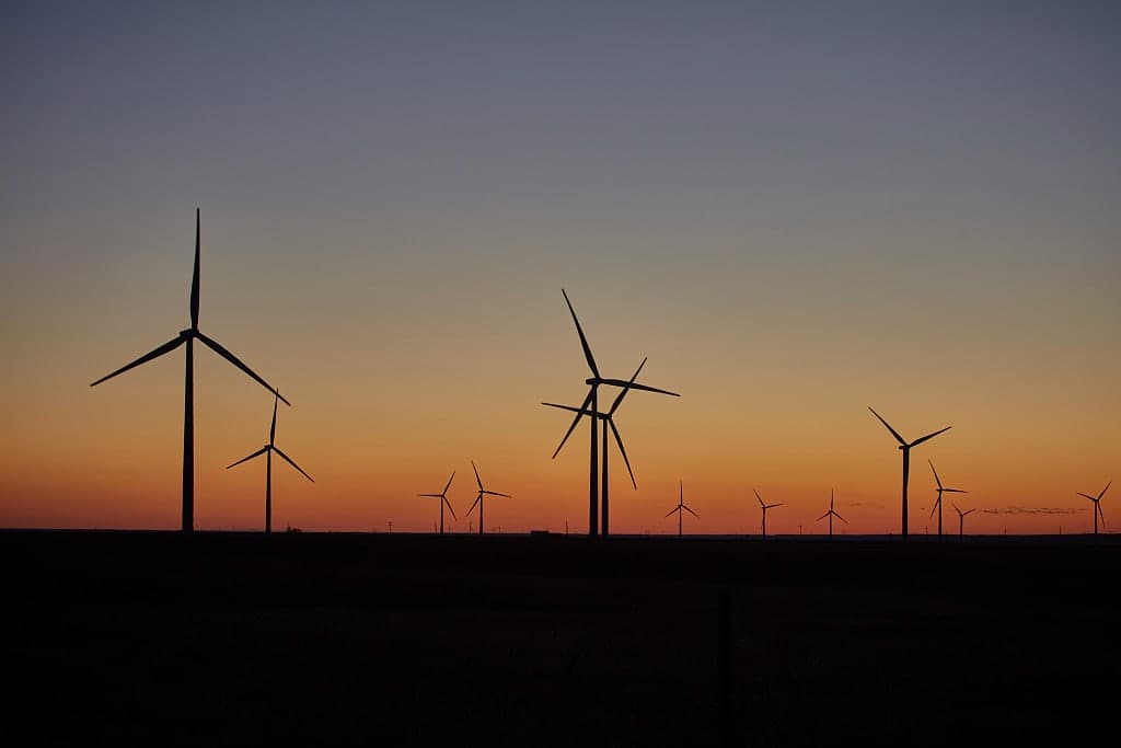 Wind turbines silhouetted against an orange sunset on the Oklahoma plains